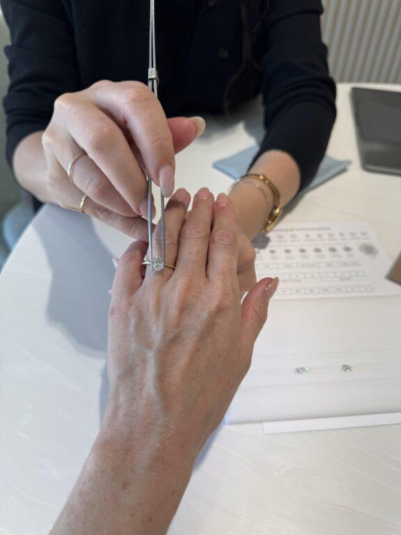 A person uses tweezers to place a gemstone on another person's finger, possibly for a ring fitting or jewelry selection.